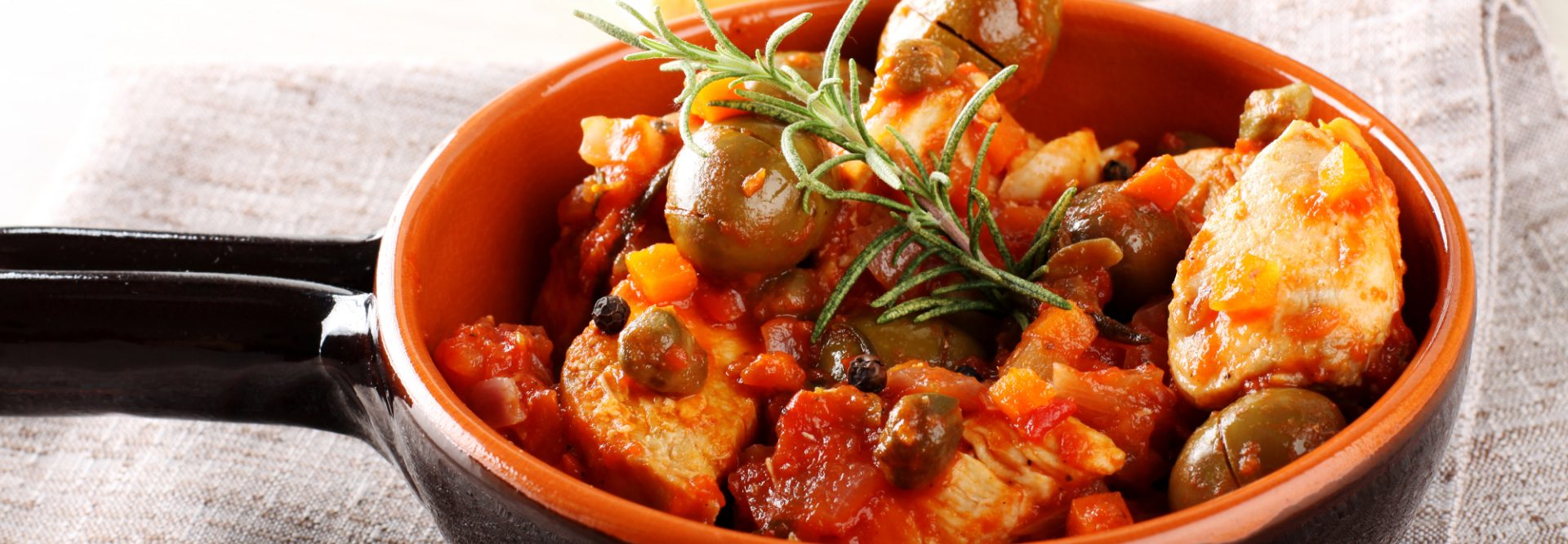 Chicken with tomato sauce, capers and olives on complex background