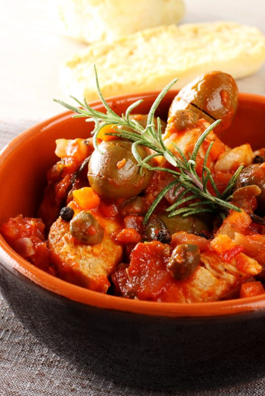 Chicken with tomato sauce, capers and olives on complex background