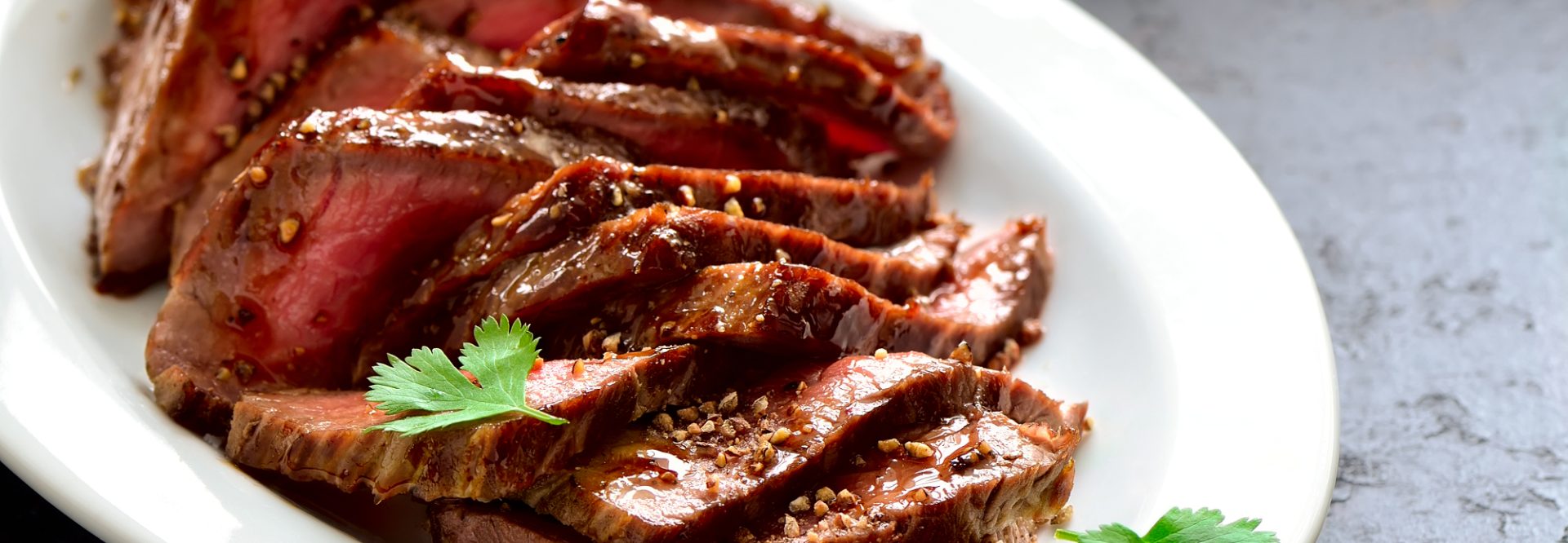 Juicy flank steak in an oval white plate decorated with cilantro leaves