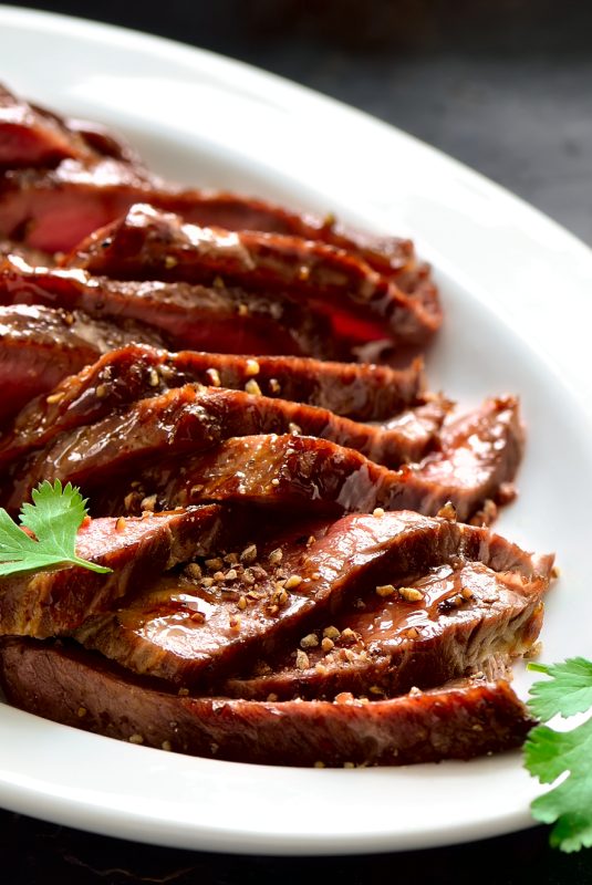 Juicy flank steak in an oval white plate decorated with cilantro leaves
