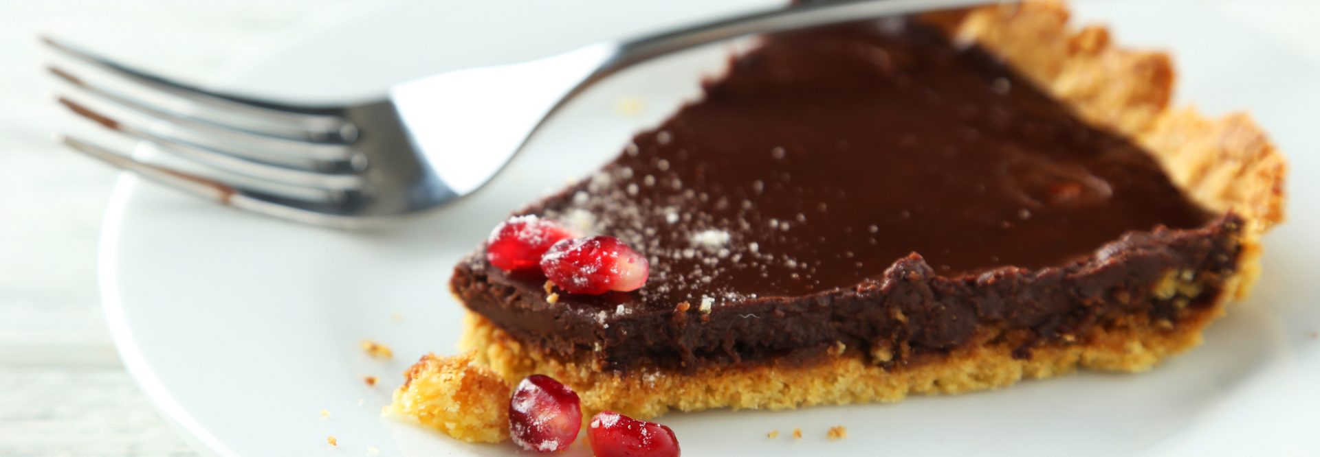Homemade chocolate tart with pomegranate on white wooden background