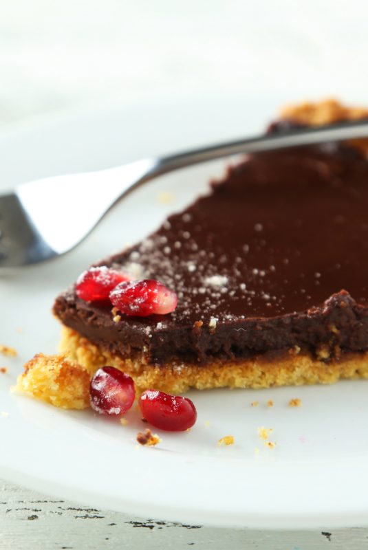 Homemade chocolate tart with pomegranate on white wooden background