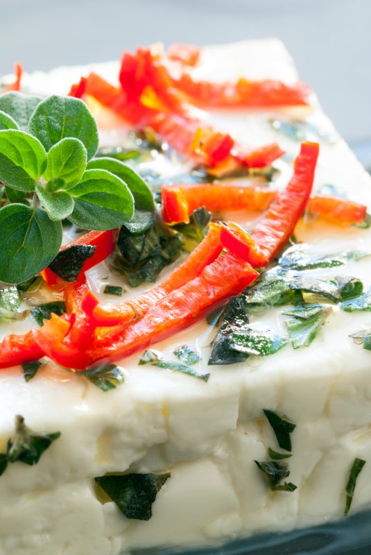 Baked feta cheese with oregano and chilli.  On dark slate.